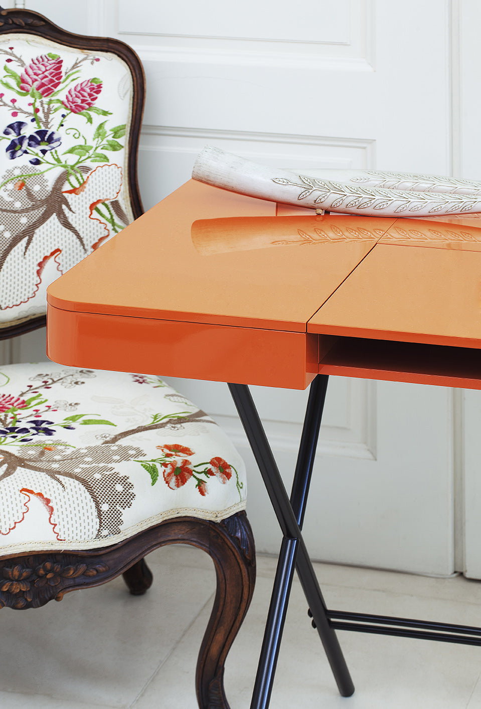 Angle arrondi du bureau Cosimo laqué orange brillant, à côté d'un fauteuil classique tapissé