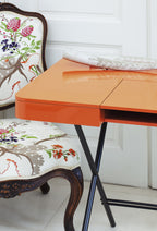 Angle arrondi du bureau Cosimo laqué orange brillant, à côté d'un fauteuil classique tapissé
